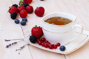 Herbal tea with lavender and mint, fresh strawberries, blackberries and blueberries on a white wooden table. Berry tea with fresh strawberry, blackberry.