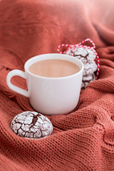 Cup of coffee with milk and chocolate cookies on warm knitted coral blanket.
