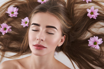 Relaxed young lady with flowers in her hair lying on white background