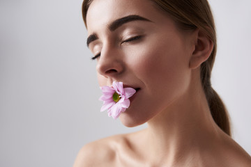 Fototapeta premium ul young lady with perfect skin holding pink flower in mouth