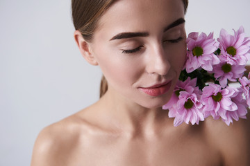 Attractive young woman keeping beautiful pink flowers on naked shoulder