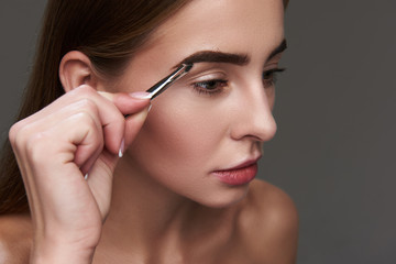 Beautiful young woman carefully plucking eyebrows with tweezers