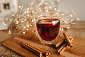 Glass of mulled wine on wooden stump with cinnamon sticks and christmas light garland