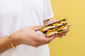 Sandwich with smoked chicken, cheddar cheese, pickled onions, pickled cucumber and sauce in male hands.