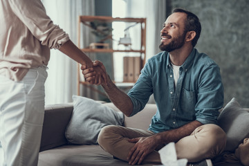Smiling man sitting on the sofa and shaking hands with woman