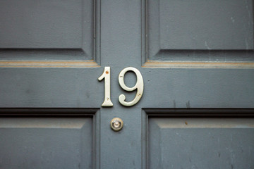 House number 19 on a gray wooden dusty door