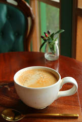 Hot coffee in a white cup with brass teaspoon served on window side's wooden table 