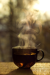 Still life cup with hot tea stands on the table against the background of a window and sunset