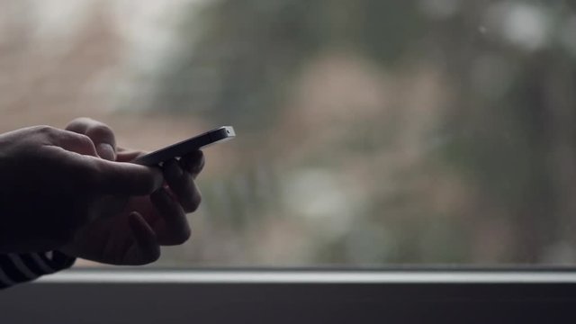 Woman using mobile phone for text messaging by the window