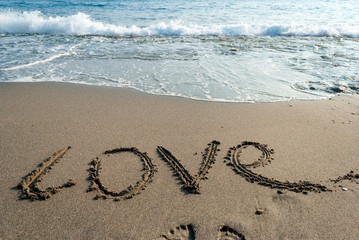 inscription love on the wet sand, a sea wave in the background