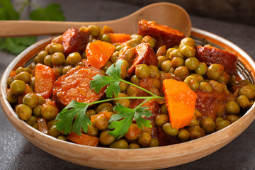 Peas stew with carrot and pork sausages in a bowl