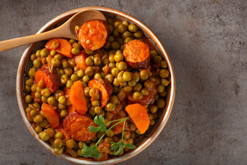 Peas stew with carrot and pork sausages in bowl with spoon