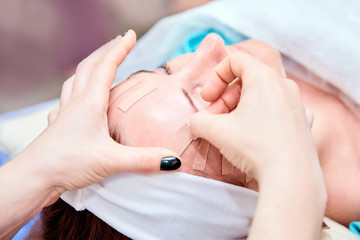 Kinesiotaping. Beautician sticking tape on the forehead of a woman. Physiotherapy and cosmetology procedure. Method of non-surgical skin rejuvenation. Facial skincare