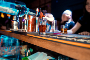 Bartender pouring strong alcoholic drink into small glasses on bar. Red shots at the nightclub. Red alcoholic drink in glasses on bar. Red cocktail at the nightclub. Barman preparing cocktail shooter