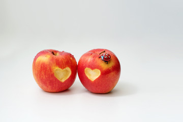 Love of two apples concept with a neatly incised heart in the skin of a ripe red apple on white table