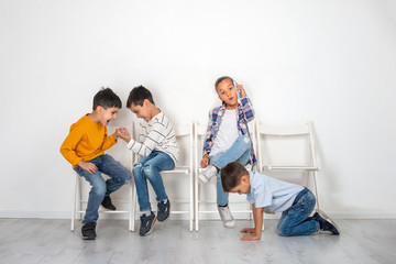 Emotional studio shot of children, girls and three boys sitting on chairs waiting. Older boys play armwrestling, the younger boy crawls on the floor and the girl chats on the phone