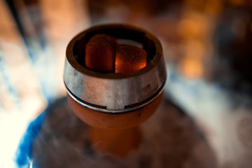 Shisha bowl with craft tobacco and red coil with hookah smoke background.