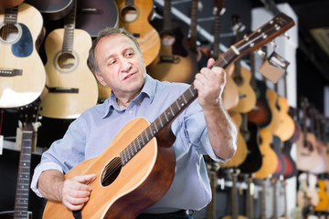 Fototapeta premium Positive male is playing on wooden acoustic guitar