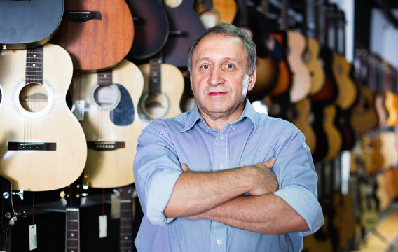 Adult guitarist is standing with acoustic guitar in music store.