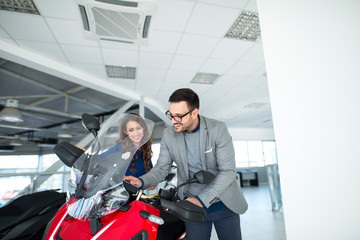 Smiling young person buying new scooter at vehicle dealership showroom.