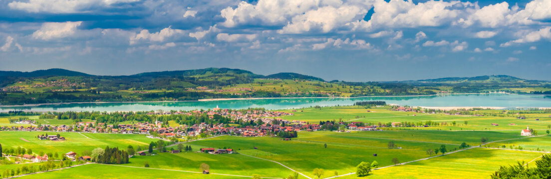A beautiful landscape panorama photo of the village Schwangau with its green fields, the turquoise blue Forggensee lake and the natural surrounding in the district of Ostallg&auml;u in Bavaria, Germany.