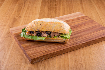 Sandwich with a cod and olives on lettuce leaves on a wooden board