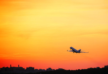 Fototapeta na wymiar Passenger plane flying over the evening city and the orange sky.