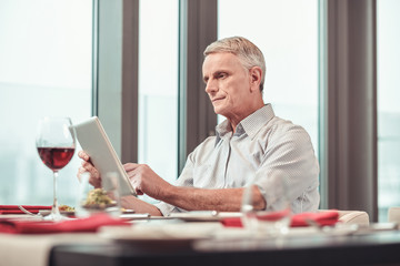Serious pensioner searching on the Internet while having lunch