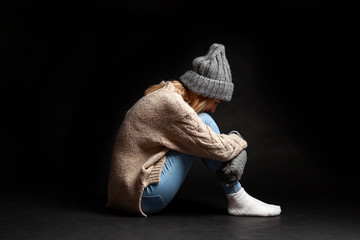 The girl is sitting alone on the floor on a black background of emptiness having embraced her legs...