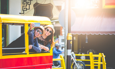 A couple of blogger tourists from Southeast Asia. Visit Phuket in Thailand are selfies on tuktuk. Captured in the old town of Phuket during write travel reviews with sunlight in travel concept .