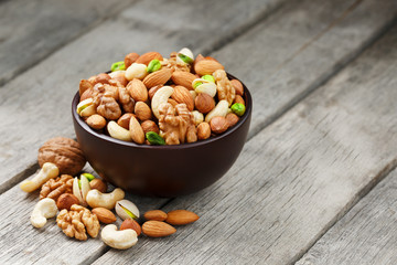 Wooden bowl with mixed nuts on a wooden gray background. Walnut, pistachios, almonds, hazelnuts and cashews, walnut.
