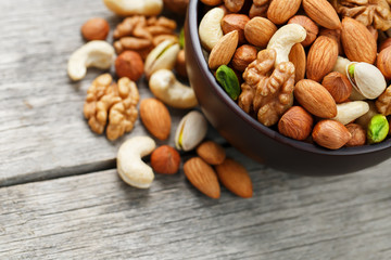 Wooden bowl with mixed nuts on a wooden gray background. Walnut, pistachios, almonds, hazelnuts and cashews, walnut.
