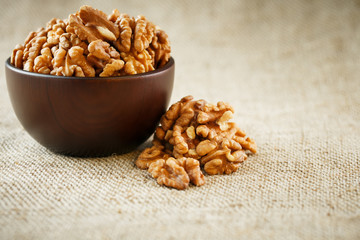 Peeled walnuts in a wooden, dark brown cup on a burlap cloth.