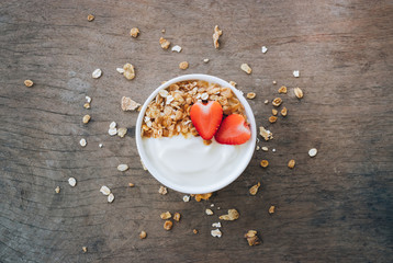 Top view of yogurt in a wooden bowl with granola,fresh strawberry on white wooden table. Health food concept.