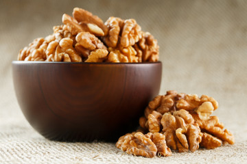 Peeled walnuts in a wooden, dark brown cup on a burlap cloth.