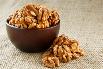 Peeled walnuts in a wooden, dark brown cup on a burlap cloth.