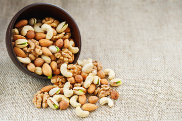 Mix of different nuts in a wooden cup against the background of fabric from burlap. Nuts as structure and background, macro. Top view.