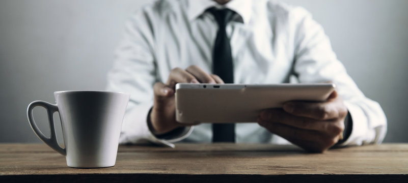 Coffee cup on table. Businessman using white digital tablet.