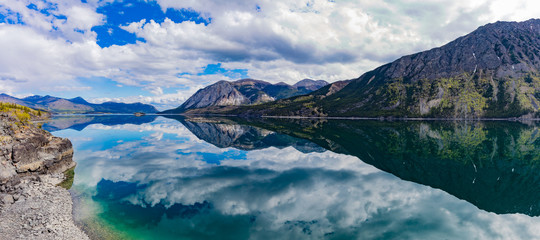 Panoramic view of calm water of Windy Arm of Tagish Lake near Carcross, Yukon Territory, Canada, with surrounding mountains mirrored on lake surface