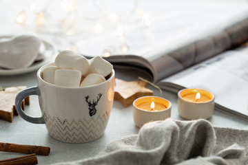 Cup of cacao, marshmallow, warm knitted sweater on grey background. Warm lights. Cozy winter. Lifestyle concept. Lifestyle rustic nordic concept