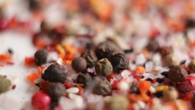 All kinds of spices fall on a white plate. Koritsa, thyme, cumin, oregano, coriander, bay leaf, basil, chili, sage, allspice, cloves, nutmeg.