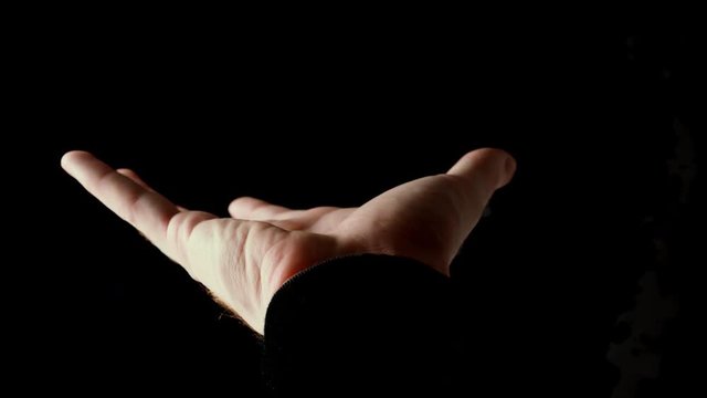 Male hand clenched infist in rays of light isolated on black background. Fingers slowly open themselves and show empty palm, then clenched back into fist. Presentation concept, slow motion video.