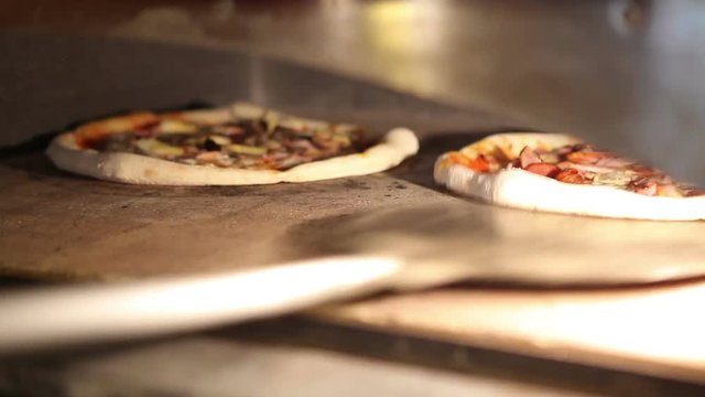 Chef pizza maker opens the oven and turns two pizzas with a shovel.