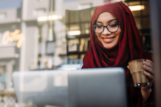 Smiling Muslim Woman Using Laptop At Cafe