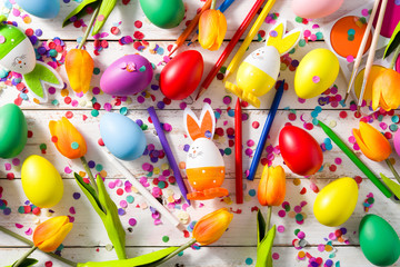 Naklejka premium Easter background with eggs, tulips and confetti on white wooden background.