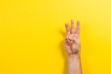 Man hand showing three fingers on yellow background. Number two symbol - obrazy, fototapety, plakaty