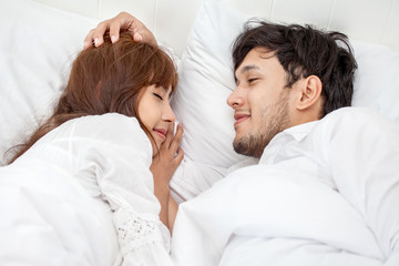 Young couple in love looking at each other lying together on white bed Romantic moment in morning to rub gently on the head