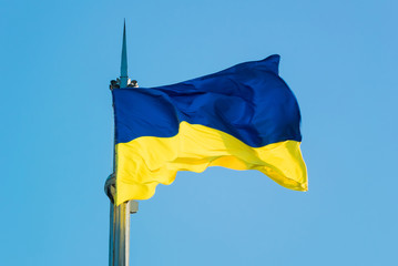 A beautiful yellow-blue Ukrainian flag develops in the wind on a sunny day against a clear sky