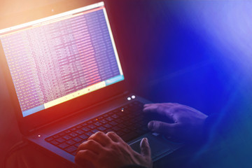 A computer programmer or hacker prints a code on a laptop keyboard to break into a secret organization system. Man hands, black background, police lights