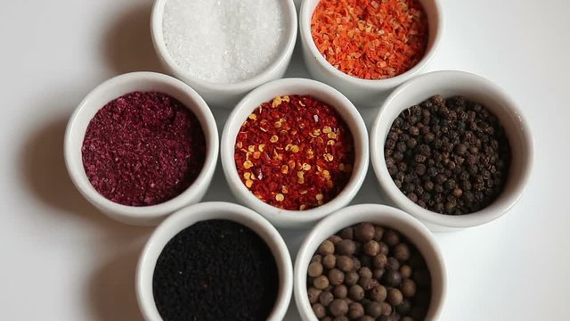 Spices and spices on the table. Black pepper peas, allspice, sea salt, red ground pepper, paprika, sumac, black cumin. Spices on a white background, rotate 360 degrees.